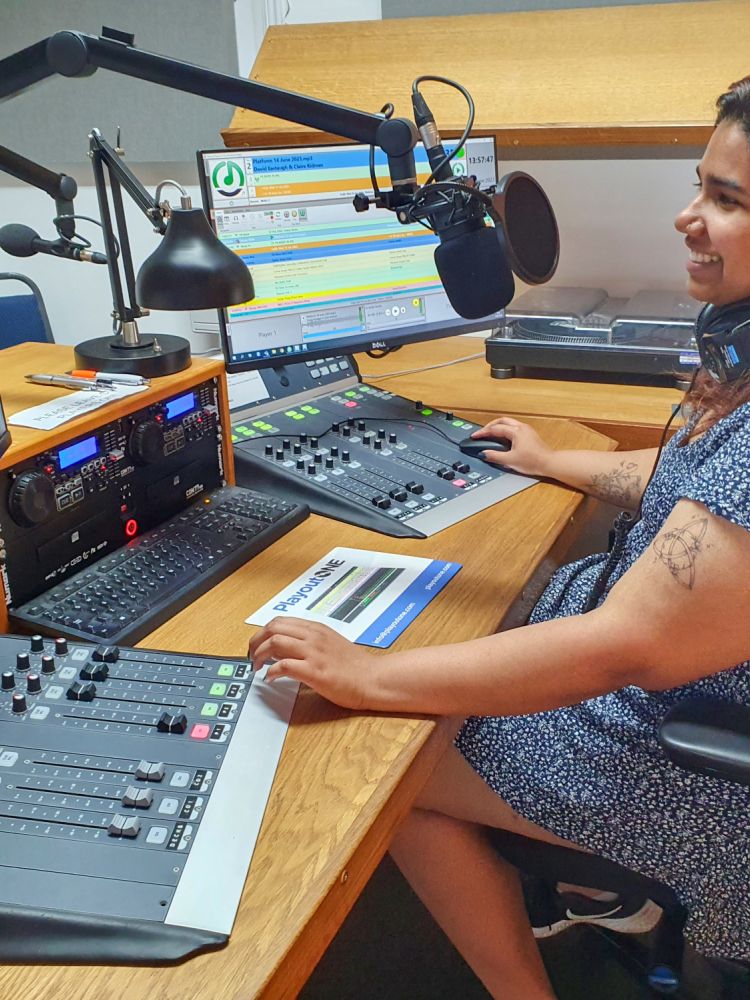 woman sat in front of a microphone at a radio station on a record your own show experience
