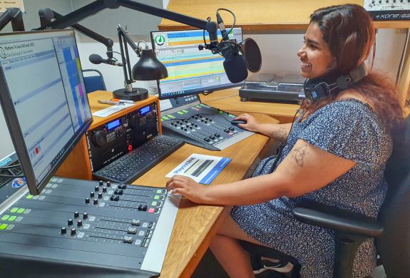 woman sat in front of a microphone at a radio station on a record your own show experience