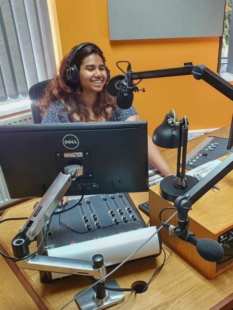 woman sat in front of a microphone at a radio station on a record your own show experience