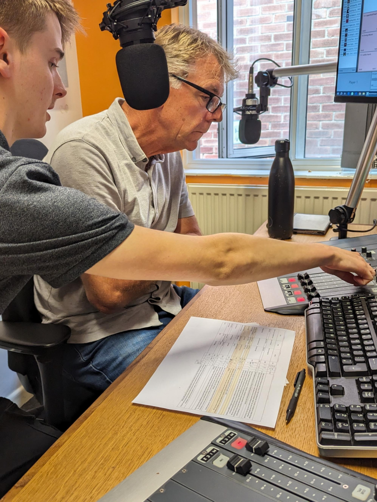 two men sat in front of a microphone at a radio station on a record your own show experience