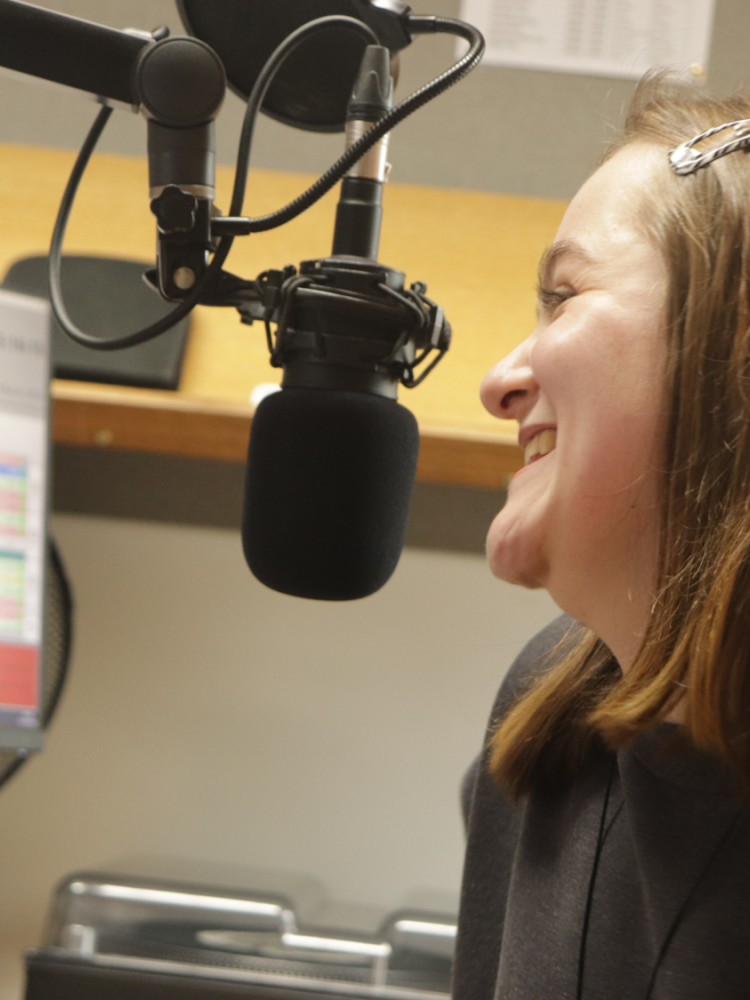 woman sat in front of a microphone at a radio station on a record your own show experience