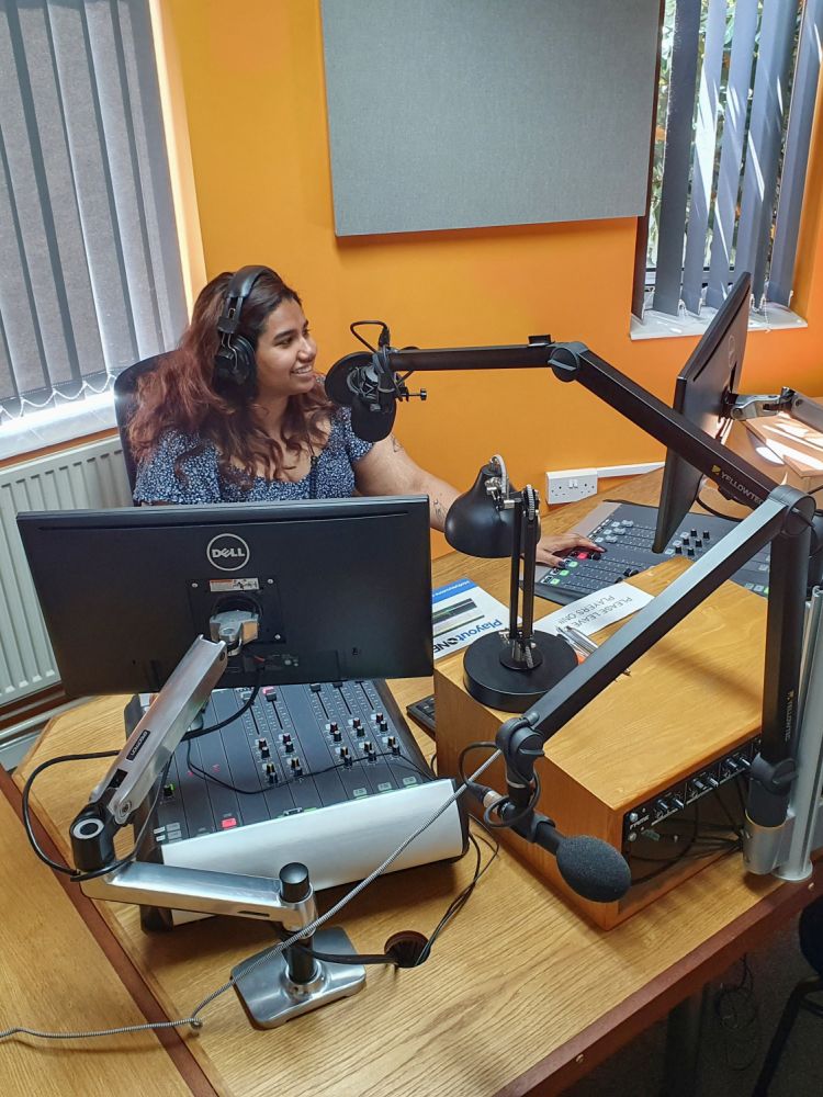 woman sat in front of a microphone at a radio station on a record your own show experience