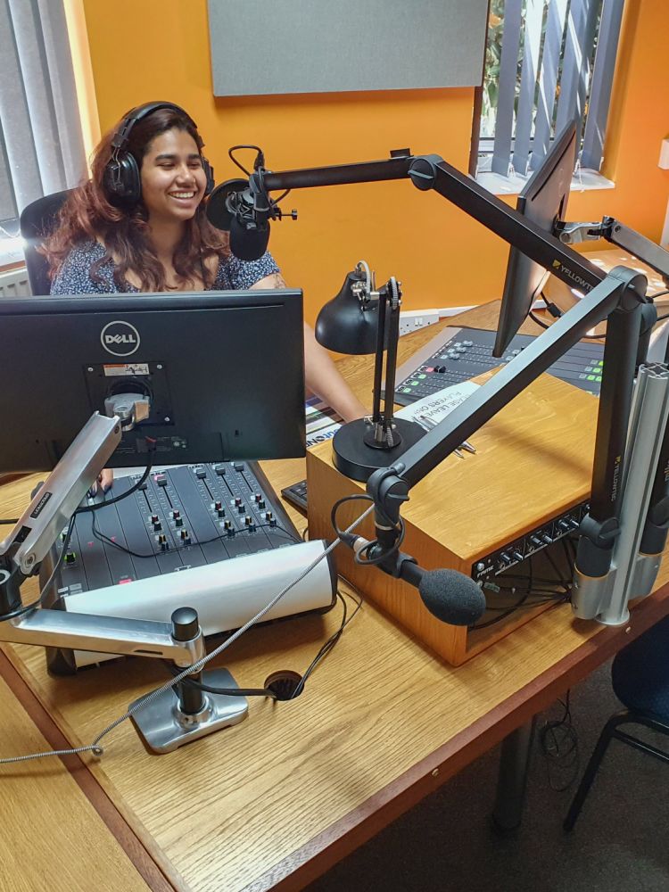 woman sat in front of a microphone at a radio station on a record your own show experience