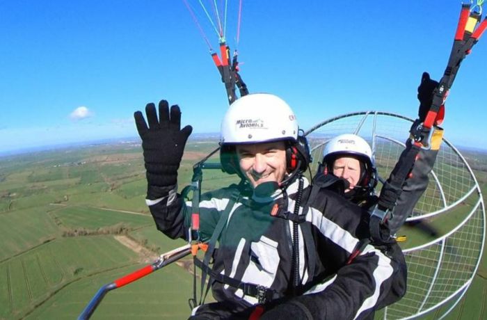 man smiling and waving while in the air on a paramotoring experience