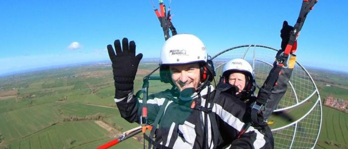 man smiling and waving while in the air on a paramotoring experience