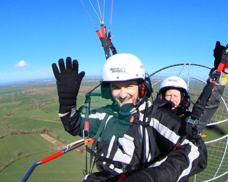 man smiling and waving while in the air on a paramotoring experience