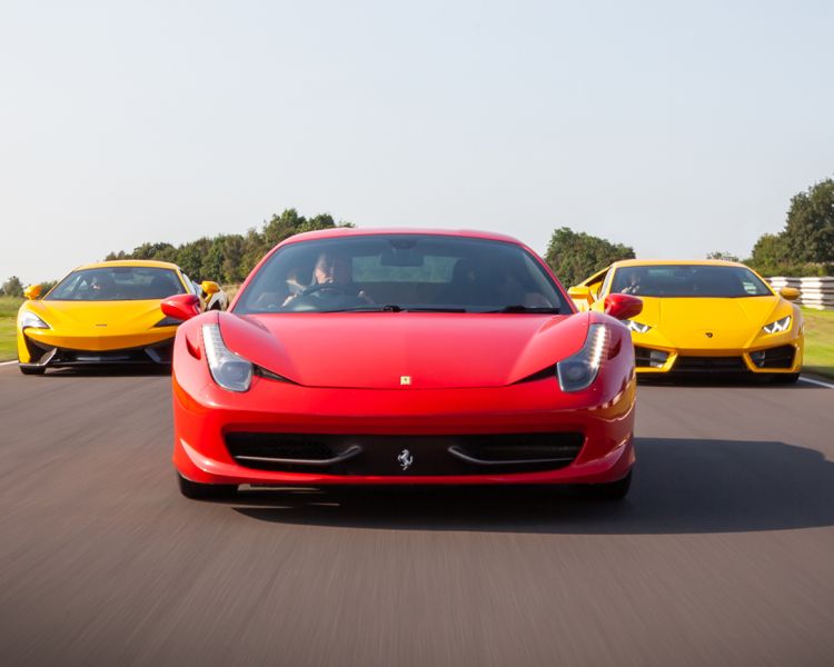 a red ferrari and two yellow lamborghinis behind it on a race track for a driving experience day