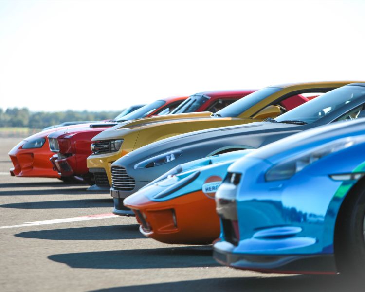 a line up of supercars and classic cars on a race track for a premium car driving experience
