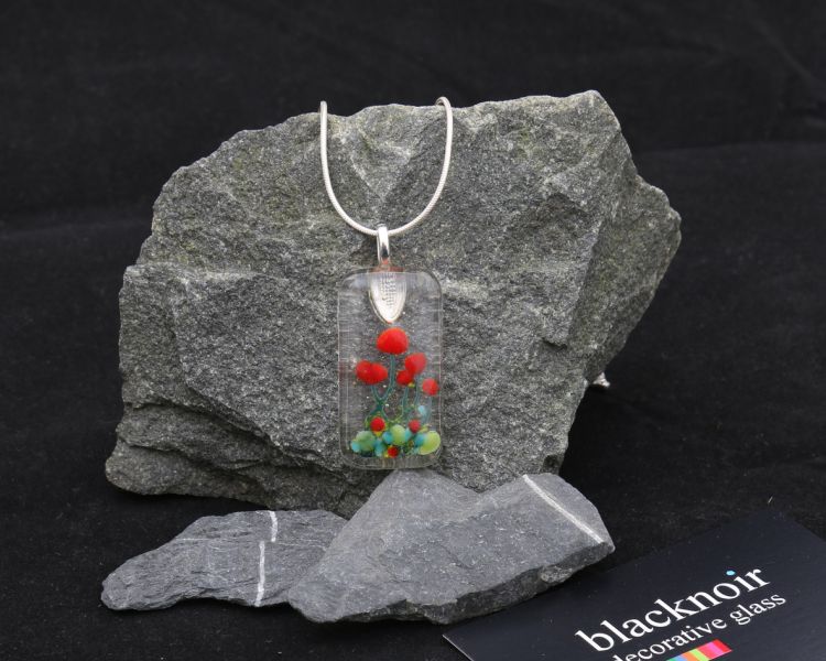 a necklace pendant made from fused glass of a poppy design resting on a stone background