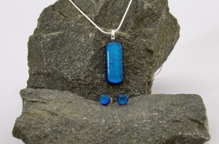 a jewellery set of necklace and earrings made from blue glass resting on a stone background