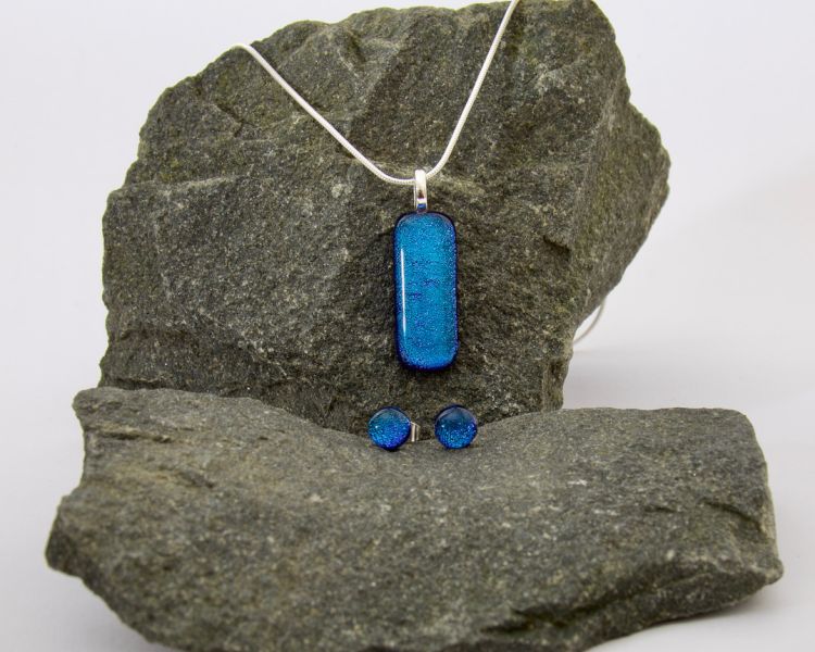 a jewellery set of necklace and earrings made from blue glass resting on a stone background