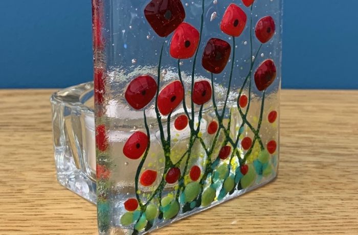 a tealight holder made of clear fused glass with a red poppy design