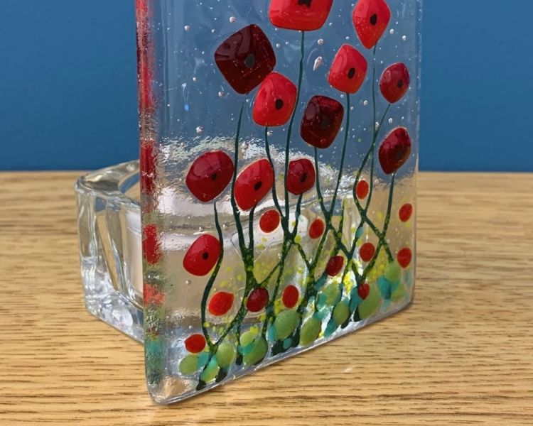 a tealight holder made of clear fused glass with a red poppy design