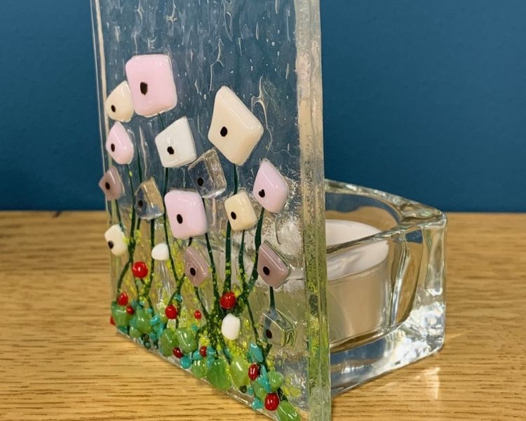 a tealight holder made of clear glass with a coloured floral design