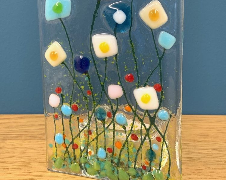 a tealight holder made of clear glass with an abstract coloured floral design on the front