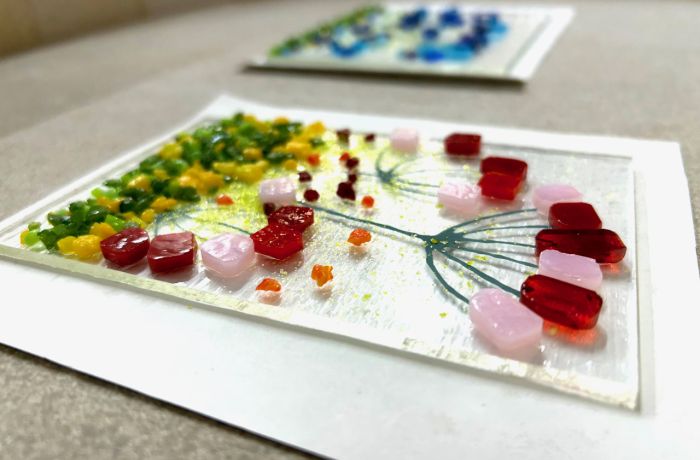the front of a glass tea light holder with a coloured floral design laid on a board ready to go into the kiln