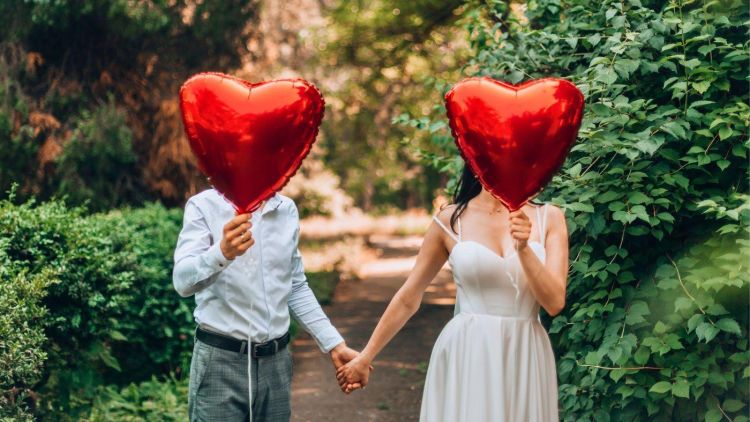 Man and woman holding red heart balloons in front of their faces