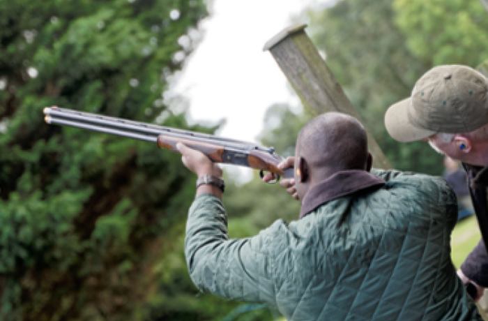 man pointing shotgun to the sky with instructor looking on as part of clay pigeon shooting experience
