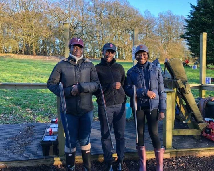 three people standing in a row smiling enjoying a clay pigeon shooting experience