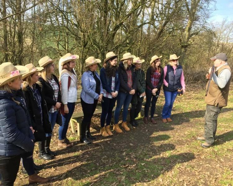 a group of people standing in a line outside listening to instructions from an instructor as part of a clay pigeon shooting experience