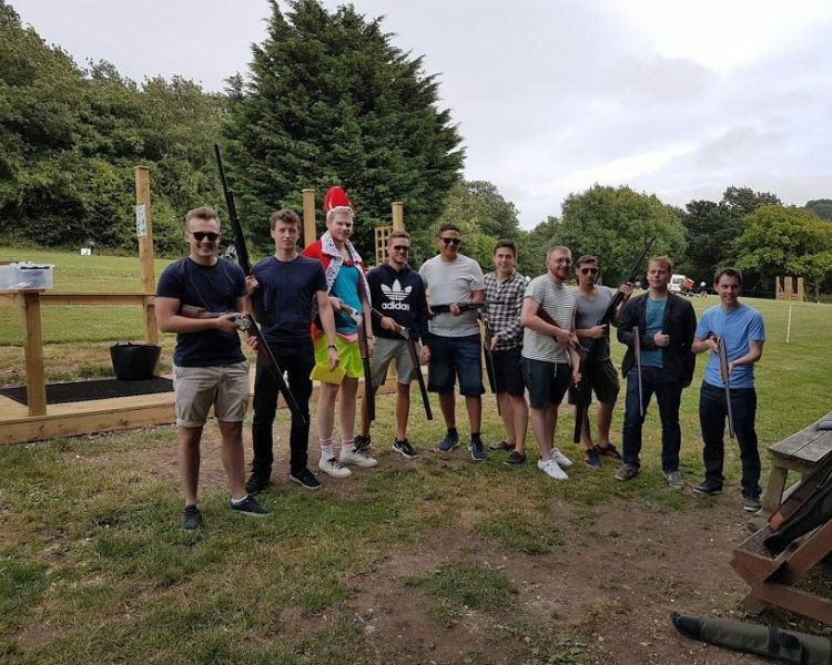 a group of men standing in a row outside holding shotguns as part of a clay pigeon shooting experience