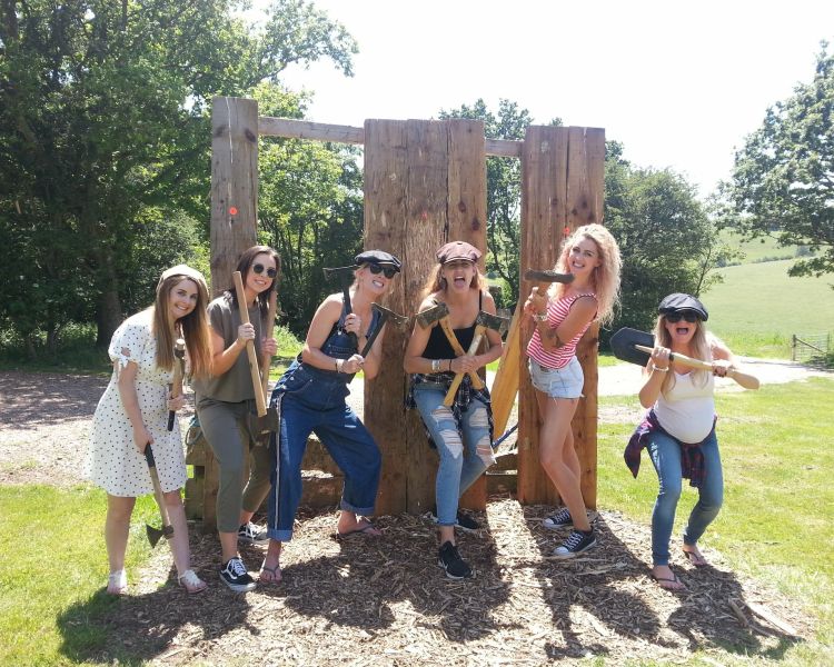 group of women posing in front of wooden boards holding axes as part of an axe throwing experience
