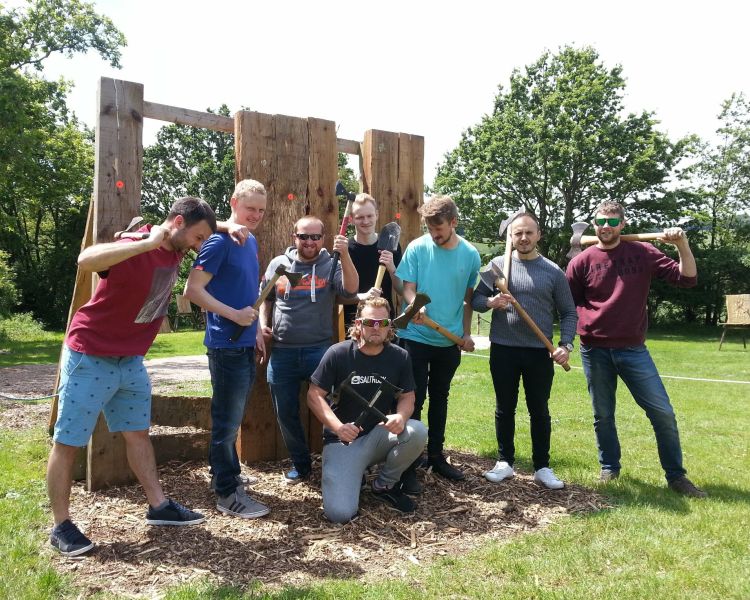 a group of men posing for a photo in front of wooden boards holding axes as part of an axe throwing experience