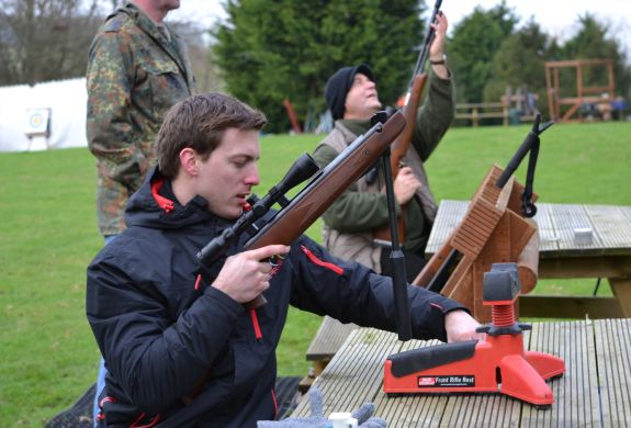 man sitting at table outside holding an air rifle as part of an air rifle shooting experience with instructor in background