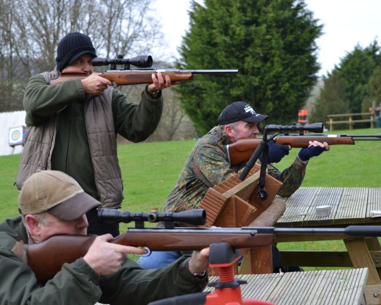 three people aiming air rifles, two are sitting and one is standing up, as part of an air rifle shooting experience
