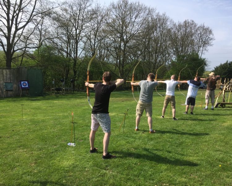 a row of people holding bows and arrows aiming at targets as part of an archery experience