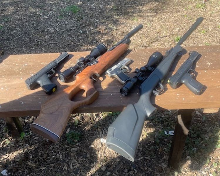 pistols and rifles on a wooden bench ready for a shooting experience