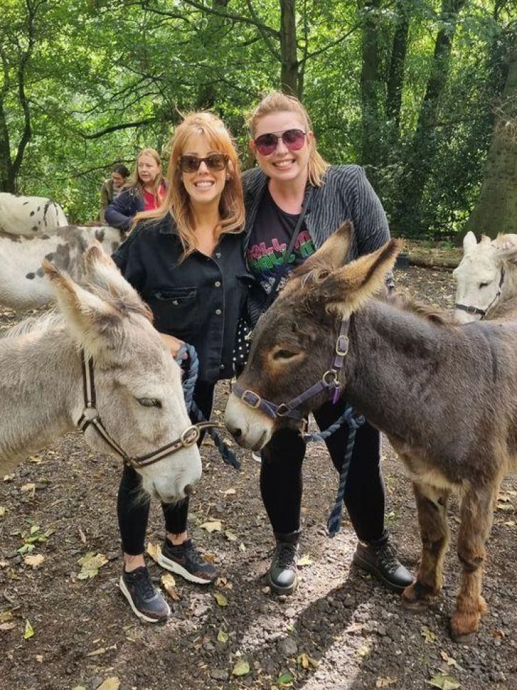 two women standing with donkeys in the woods on a donkey walk experience