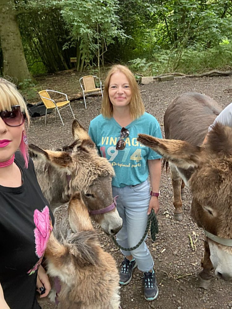 three women standing with donkeys in the woods on a donkey walk experience