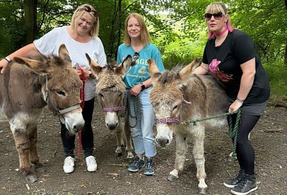 three women standing with donkeys in the woods on a donkey walk experience