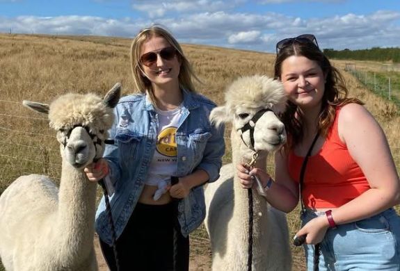 two women standing next to alpacas on an alpaca walk experience