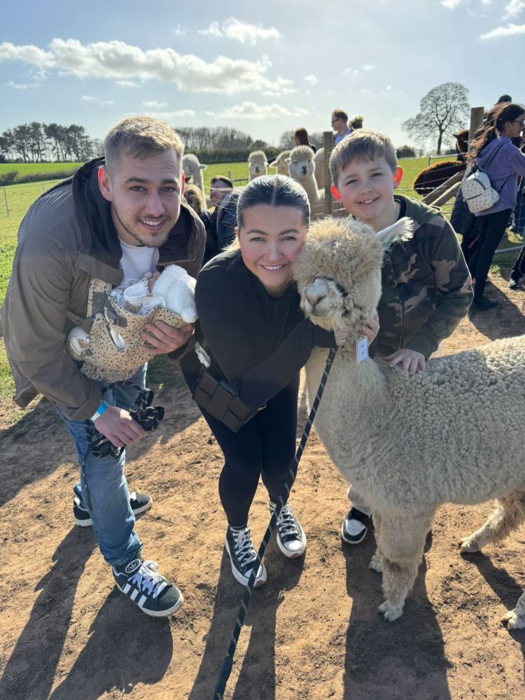 a young family having a photo taken with an alpaca on an alpaca walk experience