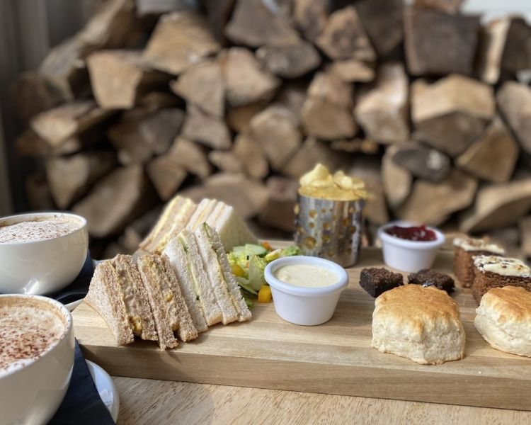 an afternoon tea spread of sandwiches scones with jam and cream on a wooden board at a farm cafe