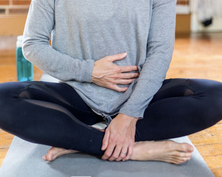 woman sitting cross legged on a yoga mat with one hand on her stomach during a meditation session on a mindfulness day retreat