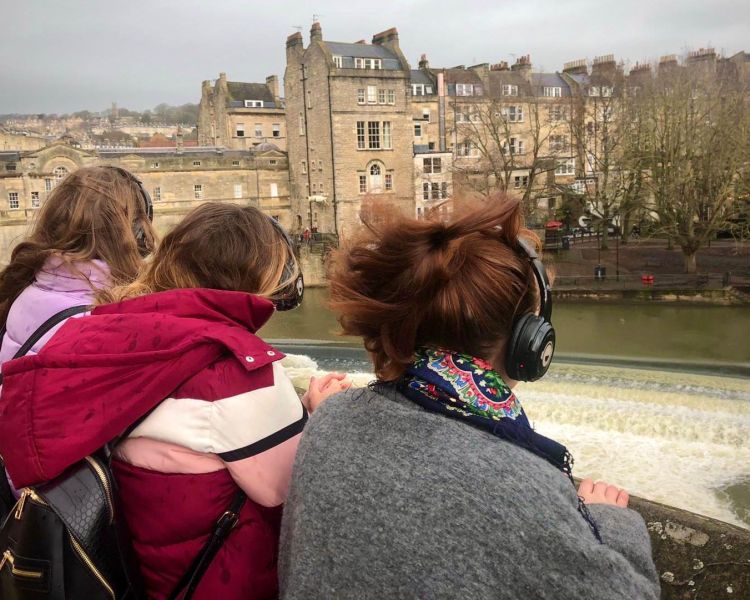 Girls wearing headphones overlooking a bridge in bath on a bridgerton walking tour