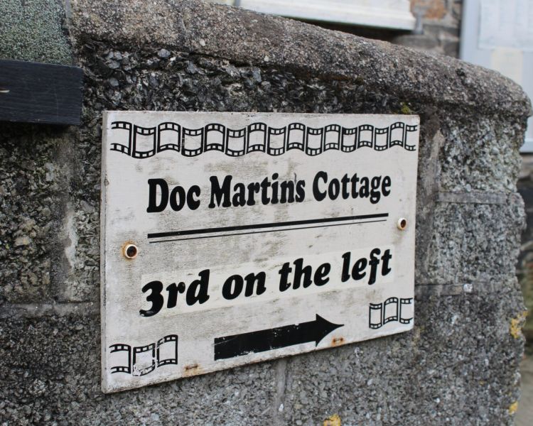 Sign on wall pointing to doc martins cottage seen on a doc martin locations tour in cornwal