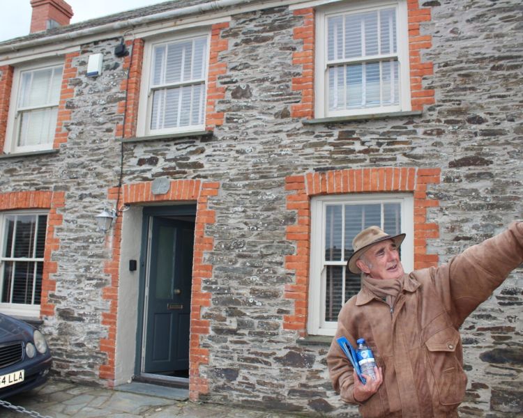Tour guide pointing in front of stone cottage on a doc martin locations tour in cornwal