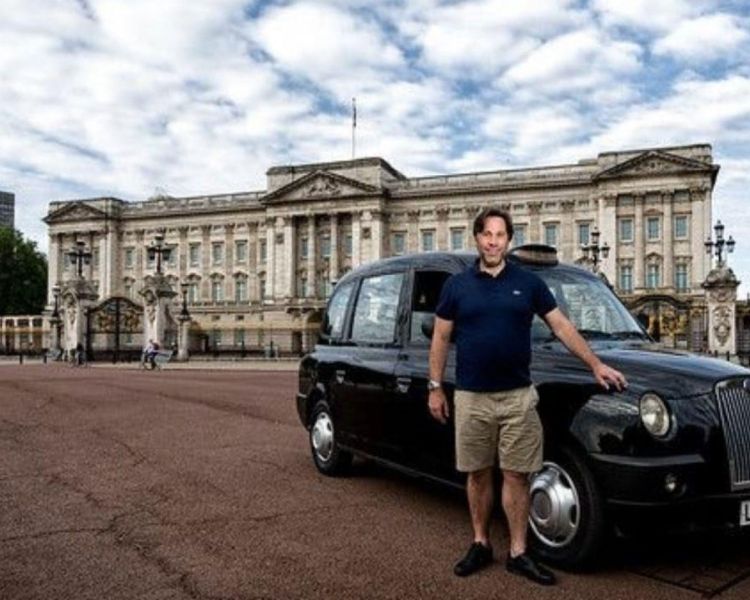 Man standing next to a back cab in front of buckingham palace