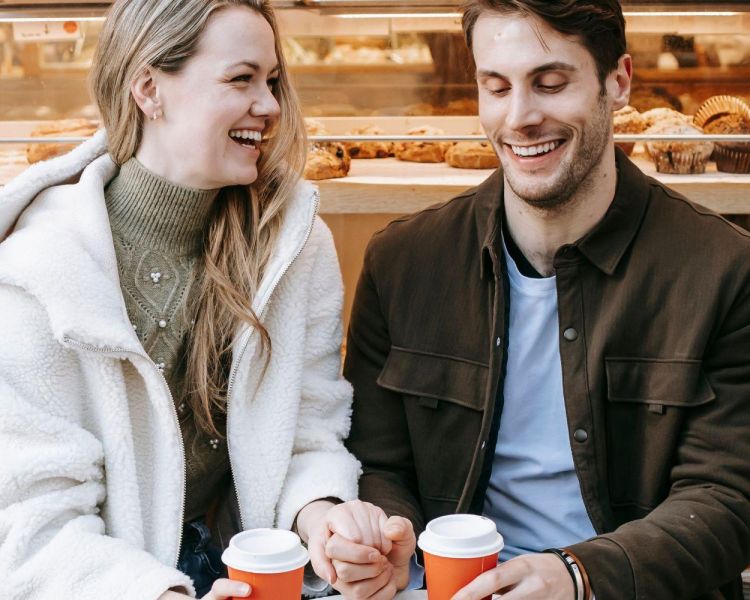 Couple holding hands drinking coffee outside bakery