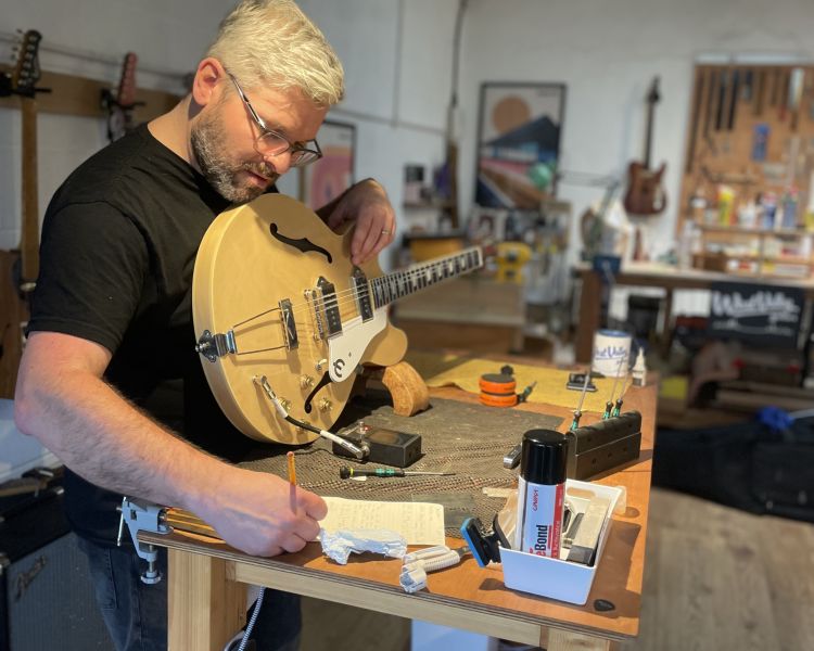 Man writing notes while holding a guitar