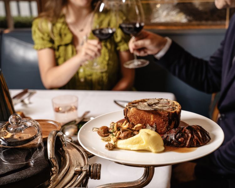 Couple clinking wine glasses having beef wellington meal at corrigans mayfair