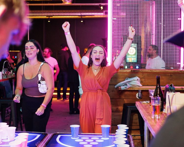 Two women playing prosecco pong in a bar