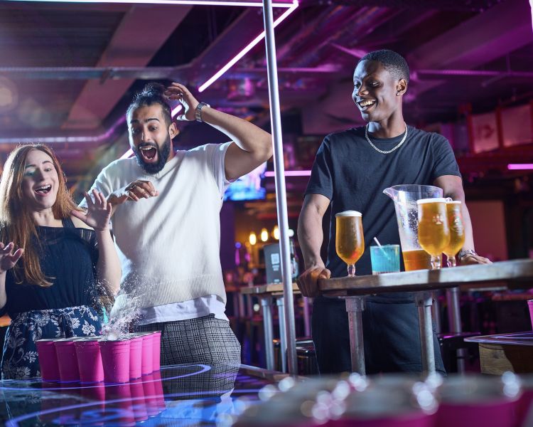 three people playing beer pong in a bar