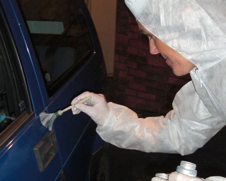 person finger print dusting on a car door as part of a crime scene investigation experience day