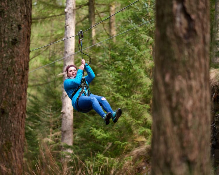 woman zip lining through trees at go ape zip trekking experience