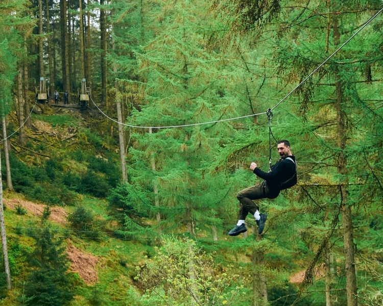 man looking back at camera whilst on zip line at go ape zip trekking adventure